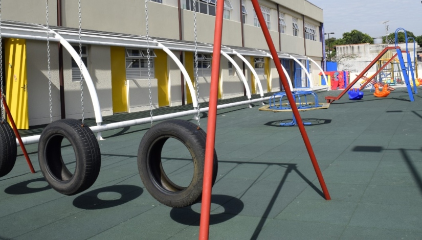 Foto de parque infantil com balanço de pneu e escorregador ao fundo