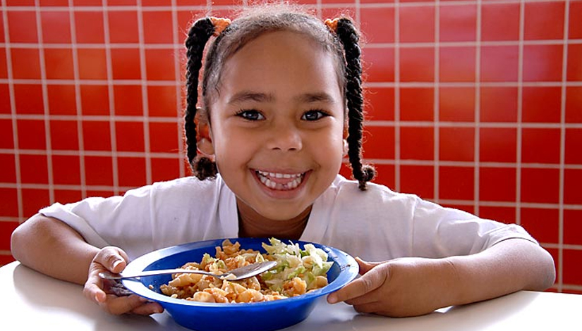 Uma menina sorrindo com o prato de merenda na sua frente.