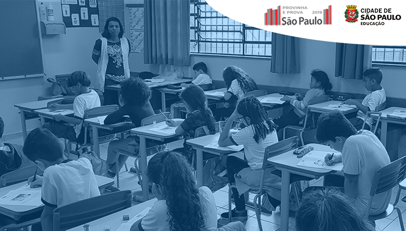 Imagem apresenta 15 estudantes em uma sala de aula fazendo prova sob a coordenação de uma professora. No topo ao lado direito, aparecem o logotipo da Provinha e Prova São Paulo e da Secretaria Municipal de Educação.