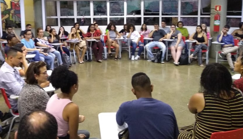 Estudantes adultos sentados em carteiras dispostas em círculo