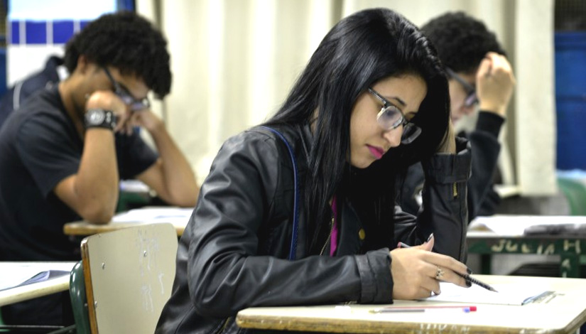Imagem mostra uma estudante realizando uma prova com um lápis na mão.