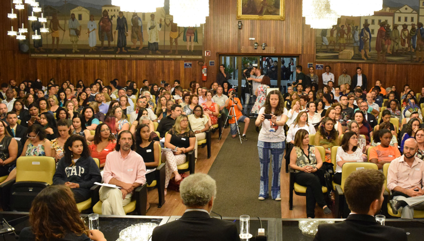Imagem mostra mais de 100 pessoas sentadas no Salão Nobre da Câmara Municipal de São Paulo participando de evento da educação.