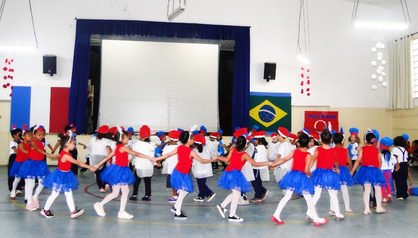 Cerca de 30 Crianças vestindo roupas nas cores azul, vermelho e branco da EMEI Montese dançando durante uma apresentação