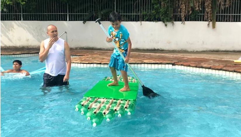 fotografia de um garoto praticando stand up padlle em uma piscina. Prancha é feita com garrafas pet