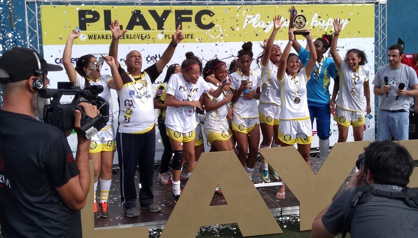 Imagem da comemoração das meninas do futebol feminino levantando o troféu.