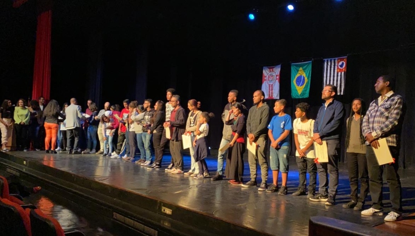 Imagem mostra estudantes e educadores no palco do auditório do CEU Alvarenga recebendo certificados.