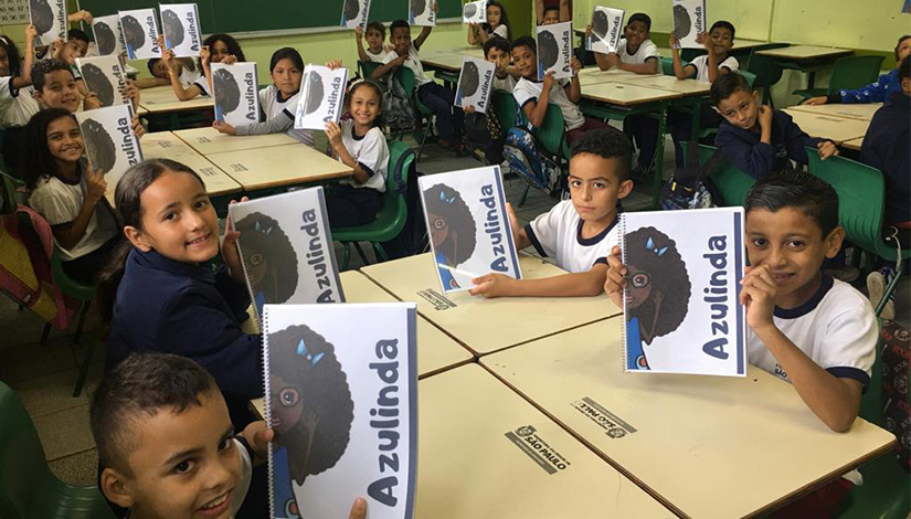 Imagem de uma sala de aula com os alunos segurando o livro "Azulinda"