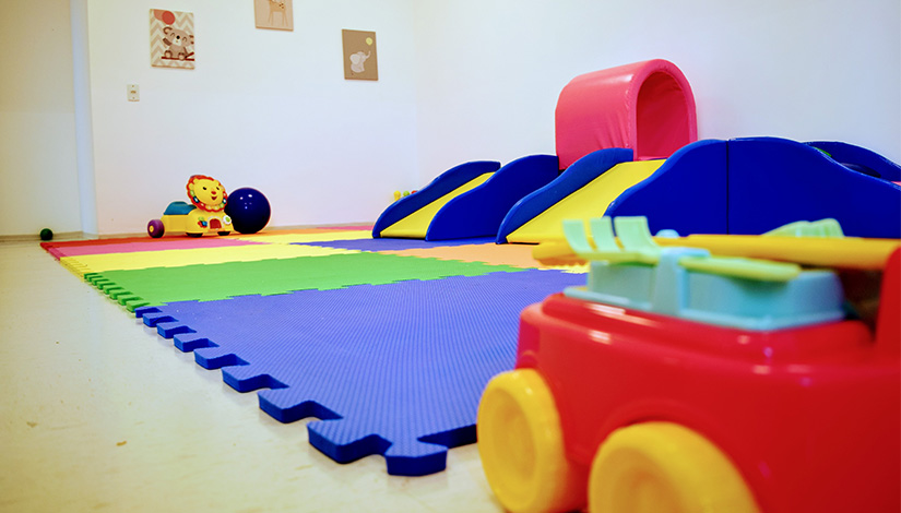 Imagem de uma sala com brinquedos e tapetes infantis no chão.