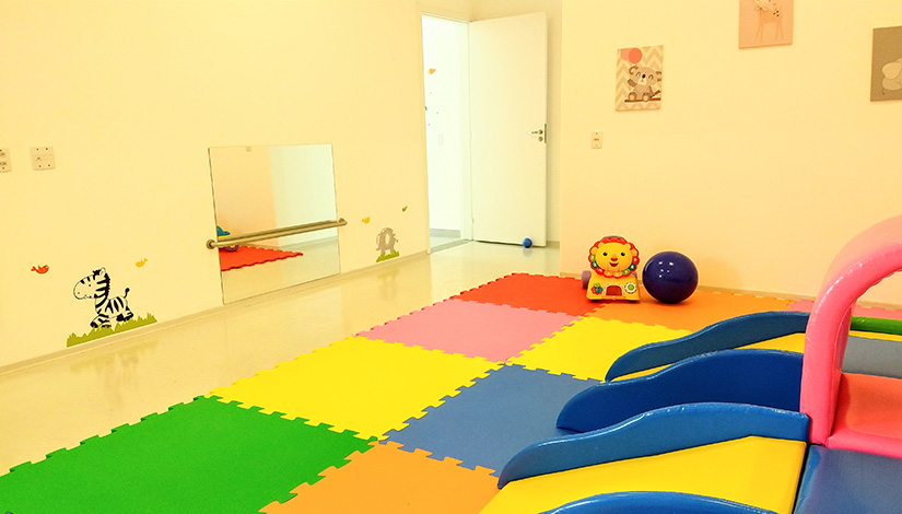 Imagem de uma sala com brinquedos e tapetes infantis no chão.