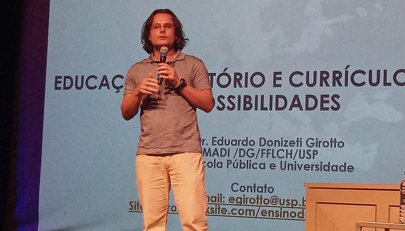 Imagem de um dos palestrantes do evento que ocorreu na DRE Pirituba - Jaraguá sobre o palco com o microfone na mão.