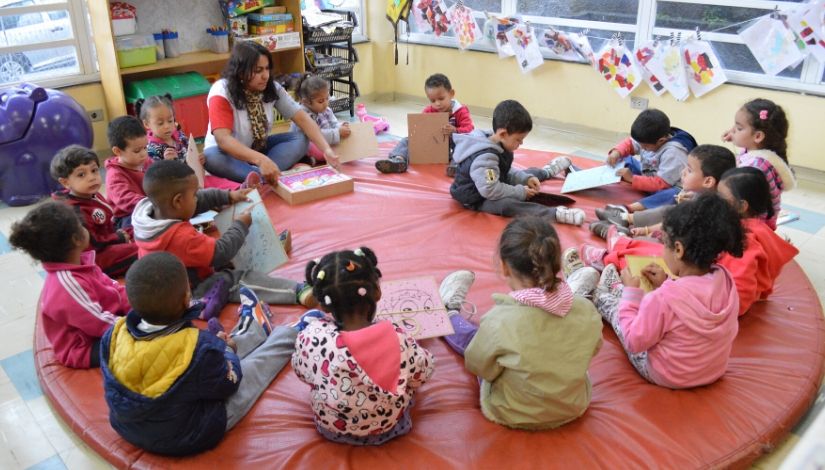 Professora e uma roda de crianças brincando com placa de costura