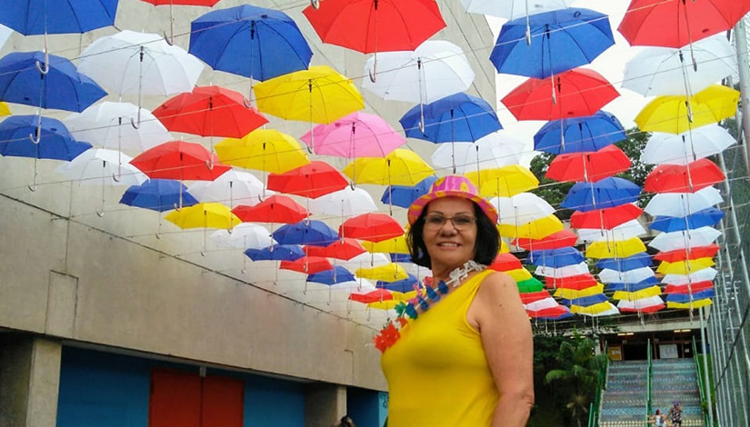 Mulher posa em frente ao corredor de guarda-chuvas coloridos instalados no CEU Alvarenga