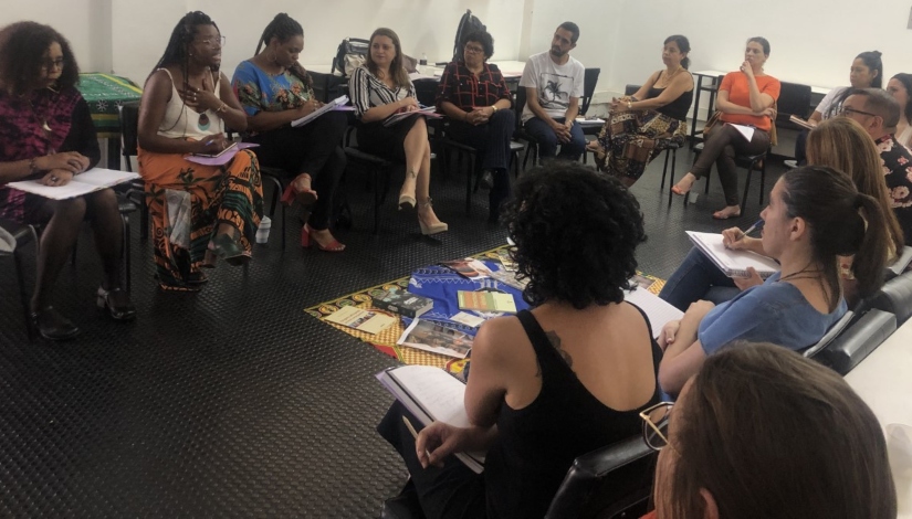 Fotografia mostra cerca de 15 pessoas sentadas em uma grande roda dialogando durante a formação.