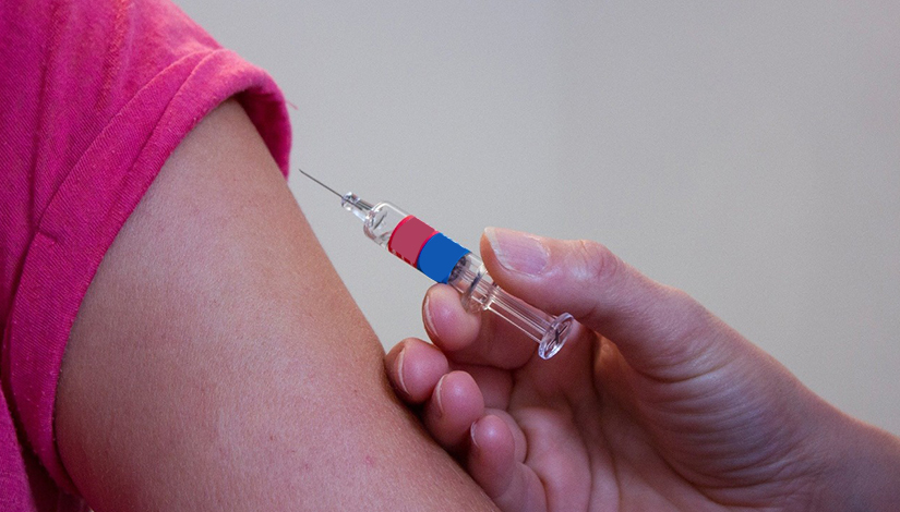 Imagem de um braço e uma mão segurando uma vacina para aplicar.