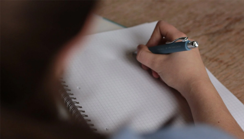 Imagem com uma mulher escrevendo em um caderno.