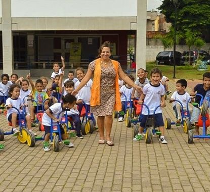 Foto De Professora E Crianças Brincando Com Triciclos Em Escola