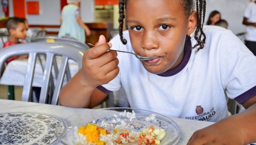 fotografia de menina com uniforme escolar se alimentando em refeitório