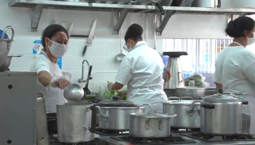 três cozinheiras trabalhando em cozinha escolar. todas utilizam máscara