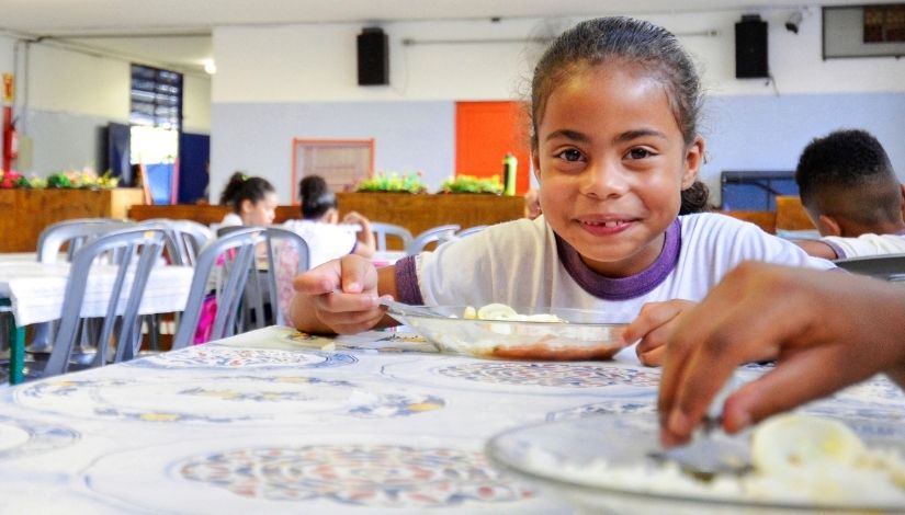 Imagem mostra estudante no momento de alimentação no refeitório de uma escola municipal