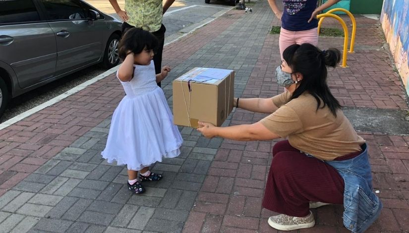 Professora entregando uma grande caixa para uma pequena menina