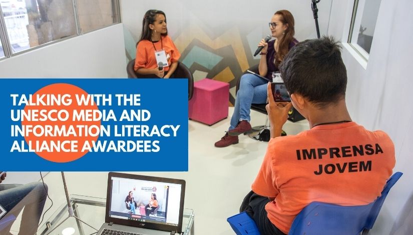 Fotografia de estudantes do Projeto Imprensa Jovem entrevistando uma pessoa em um estúdio. Imagem segue com banner do evento da unesco "talking with the unesco media and information literacy alliance awardees"