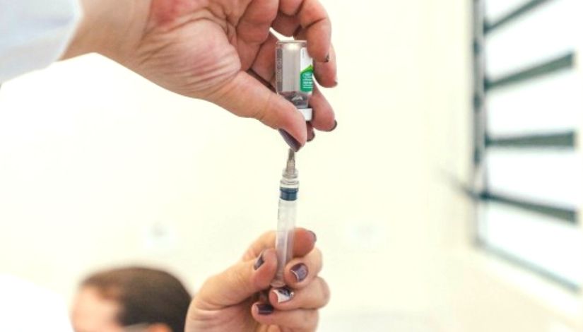 Vacina sendo preparada com agulha introduzida no frasco para aspirar a medicação.