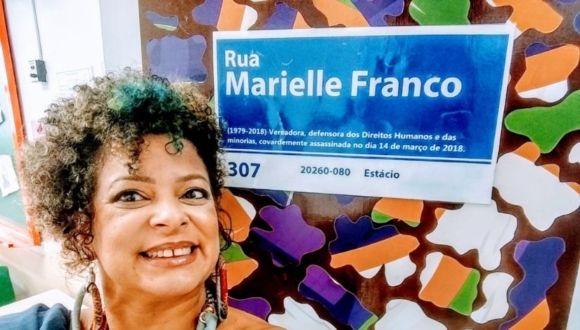 Imagem mostra professora, ao fundo placa de identificação da Rua Marielle Franco.