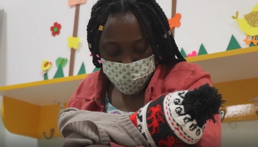 Fotografia de uma mãe amamentando seu bebê em um espaço interno do Centro de Educação Infantil.