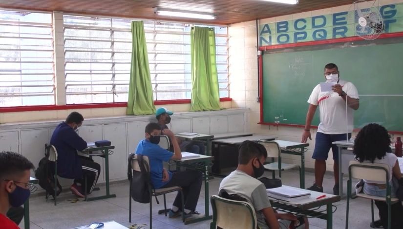 Professor e estudantes em sala de aula. Todos estão usando máscara de proteção individual.