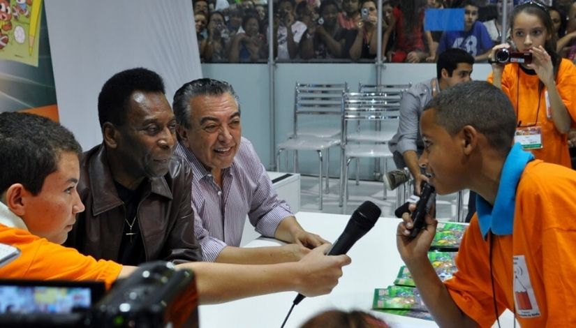 Fotografia mostra estudantes do projeto Imprensa Jovem entrevistando Pelé e Mauricio de Sousa.