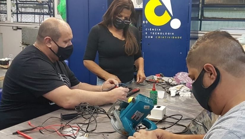 Estudantes e professor do curso de elétrica. Eles estão olhando e manuseando os equipamentos elétricos sob a mesa.