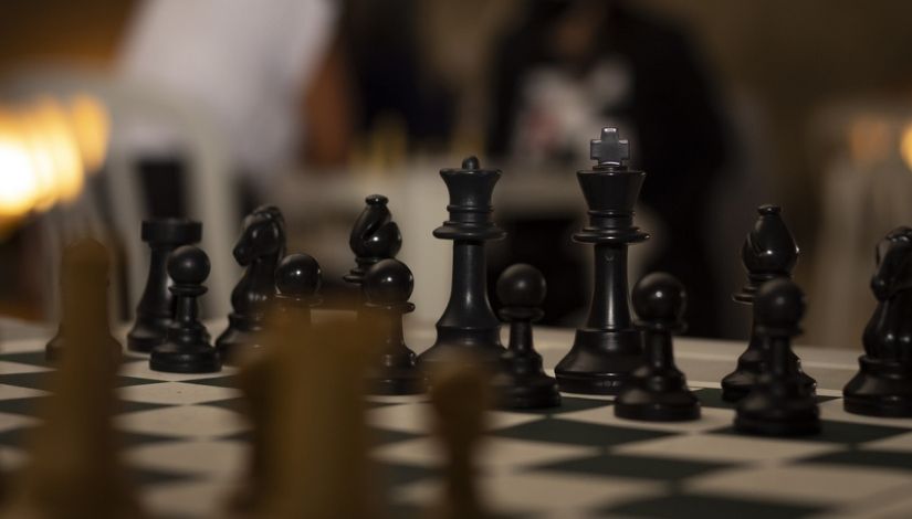 Fotografia de um tabuleiro de xadrez com foco nas peças pretas que estão centralizadas da imagem.