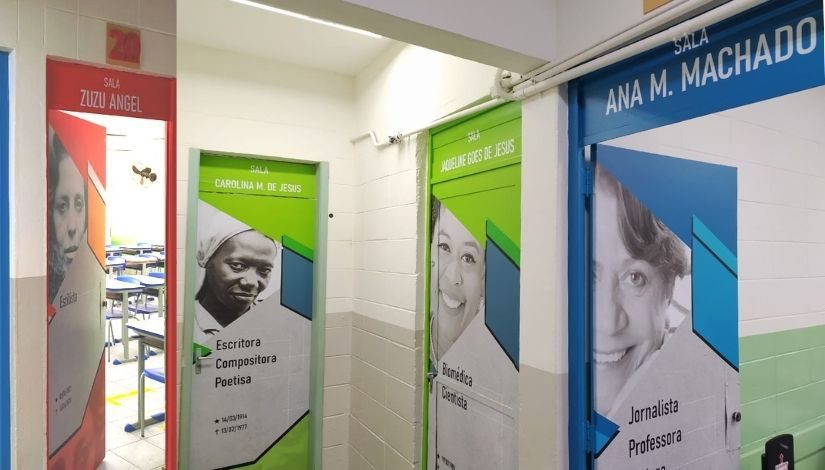 Imagem mostra quatro portas de salas de aula. A primeira delas é vermelha e está escrito "Sala Zuzu Angel" na parte superior, além de uma foto da estilista. A segunda e terceira tem a cor verde, sendo das salas "Carolina Maria de Jesus" e "Jaqueline Goes de Jesus". A quarta porta é na cor azul e está escrito "Sala Ana M. Machado"