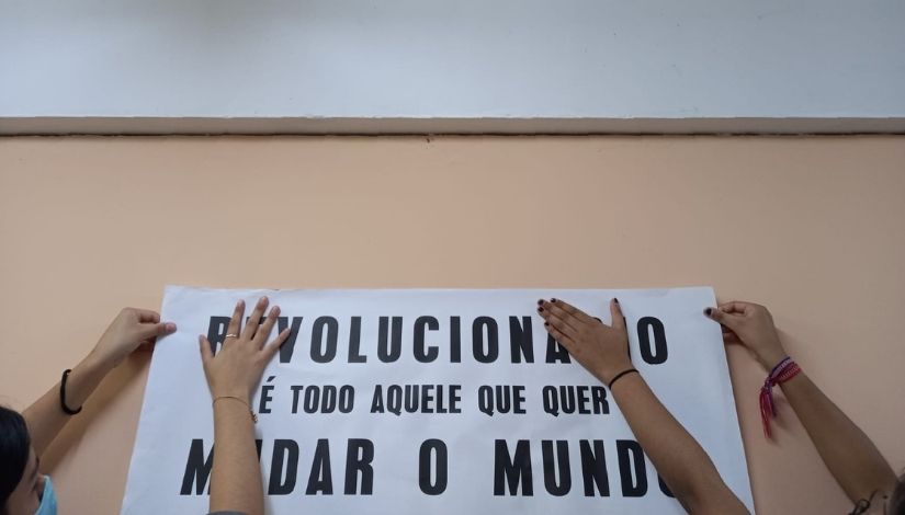 foto de cartaz com poesia sendo colado na parede por duas pessoas
