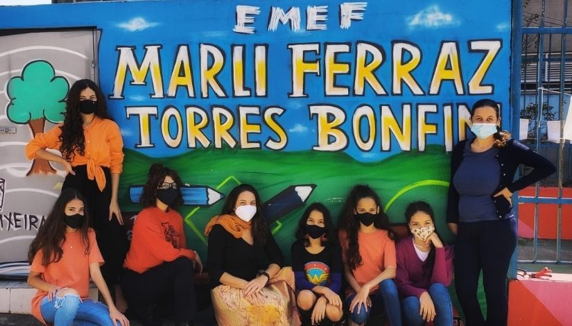 foto de grupo de seis estudantes com duas professores na frente um muro escrito EME Marli Ferraz Torres Bonfin 
