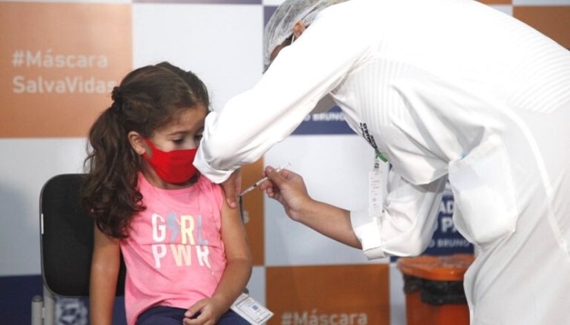 menina sendo vacinada por uma enfermeira em sua escola 