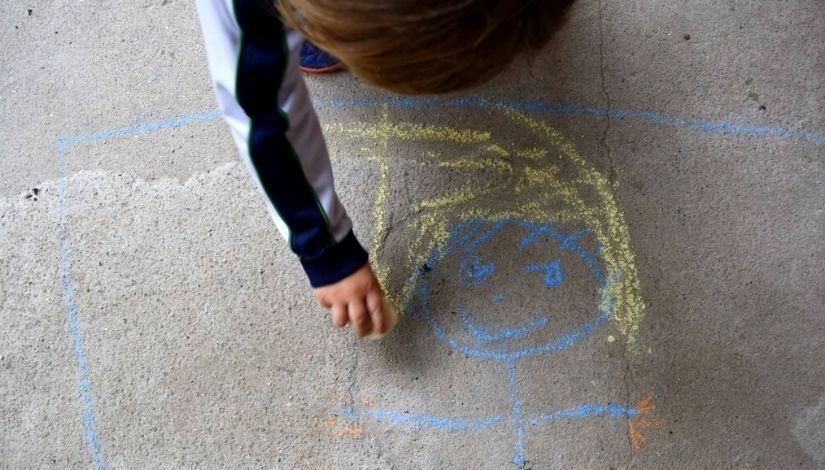 Criança desenhando com giz de lousa no chão.