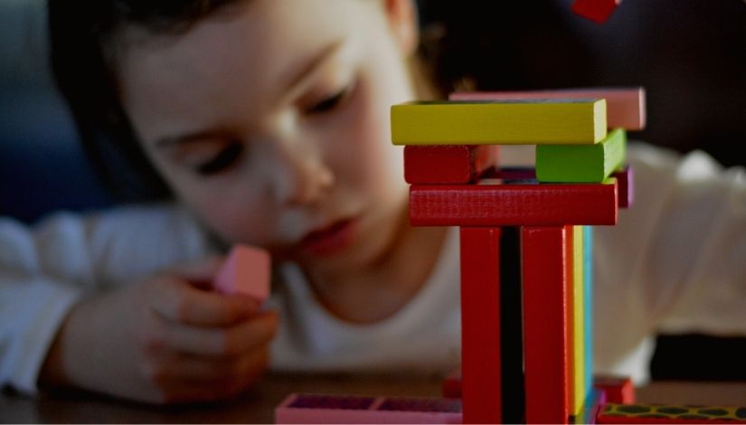 Fotografia de criança mexendo com blocos de madeira coloridos