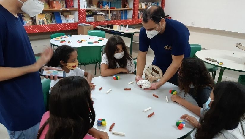 Ambiente escolar com uma pessoa adulta mostrando uma réplica de um cérebro para um grupo de estudantes.