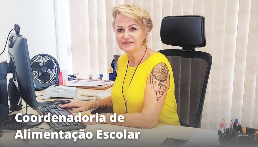 Fotografia de uma mulher loira com cabelos curtos sentada em uma meses de escritório. Coordenadoria de Alimentação Escolar