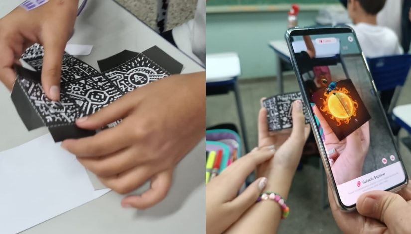 Metade da imagem mostra as mãos de uma criança dobrando um cubo, na outra metade a imagem mostra as mãos de uma criança segura o cubo e um celular apontado para o cubo com aplicativo de realidade aumentada mostrando o sol.