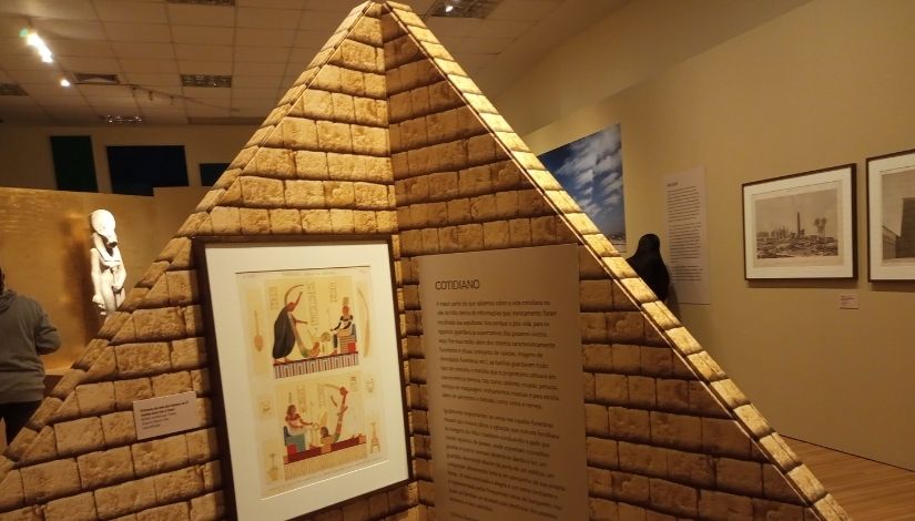 Fotografia de uma réplica de uma pirâmide, mostrando um cartaz e um quadro.