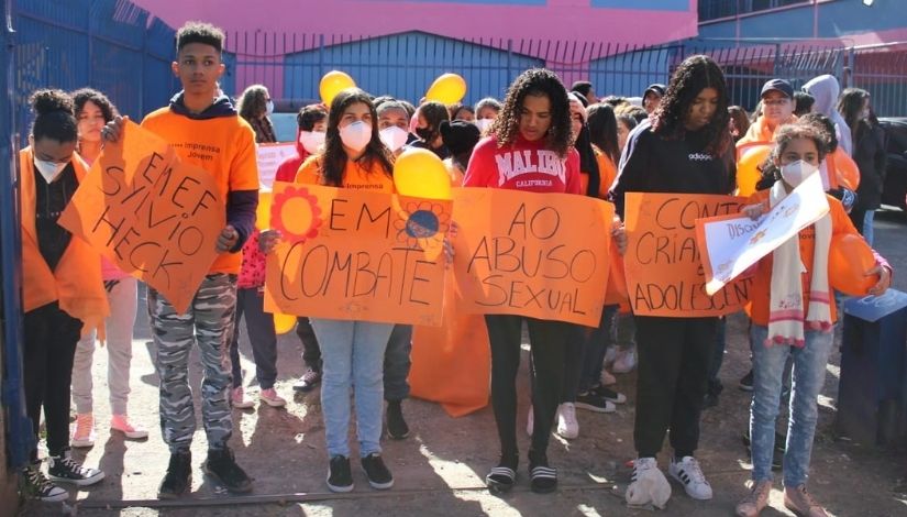 Estudantes se organizando para passeata. Ne frente do grupo, quatro meninas e um menino carregam cartazes com os dizeres "EMEF Sylvio Heck em combate ao abuso sexual contra crianças e adolescentes".