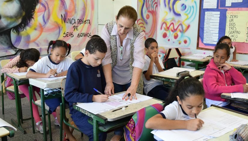 Fotografia de uma professora em sala de aula com estudantes.