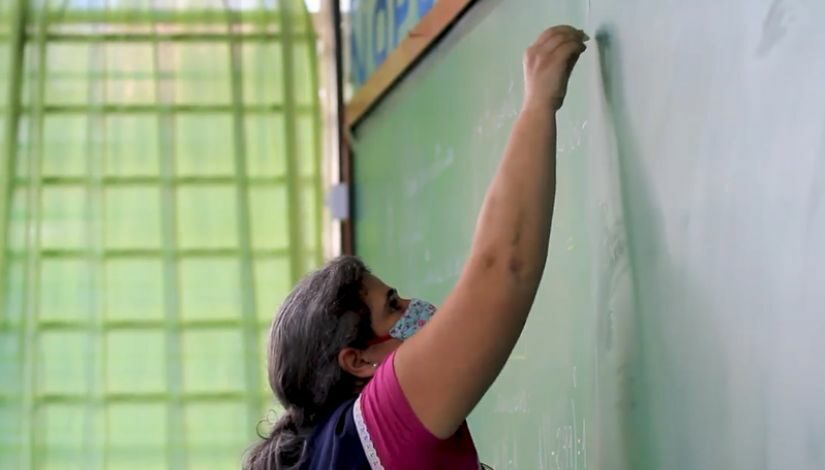 Fotografia de uma professora escrevendo na lousa.