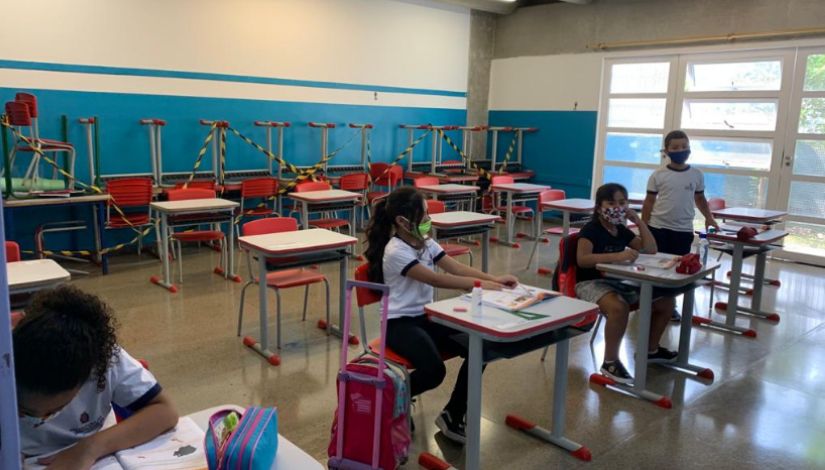 foto de estudantes com máscara na sala de aula. ao fundo, cadeiras interditadas