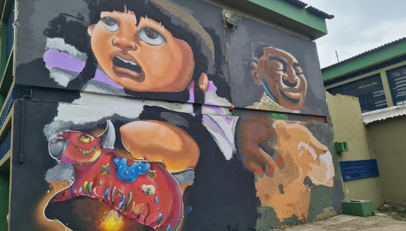 Fachada da escola com grafites que representam uma pessoa negra, uma criança com traços andinos e um bumba meu boi
