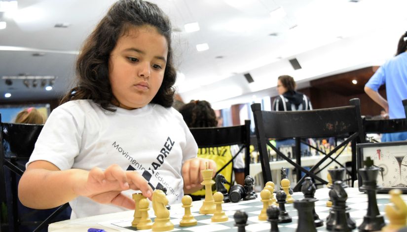 Menina jogando xadrez. Ela olha concentrada para o tabuleiro.