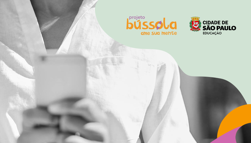 Imagem de uma pessoa do pescoço até o começo do tórax. Ela está segurando um celular. No canto superior direito seguem as logomarcas "Projeto Bússola - Ame a sua Mente" e "Cidade de São Paulo - Educação".