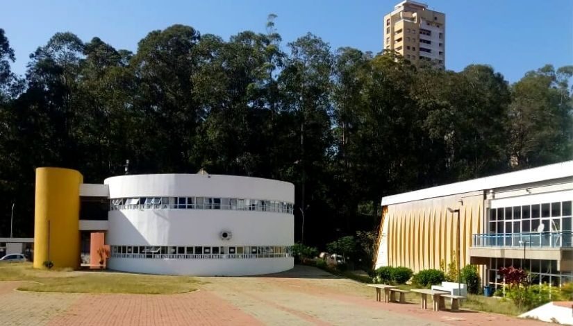 Fotografia da fachada do CEU Paraisópolis, onde mostra um prédio redondo e outro retangular na lateral, com faixas coloridas na frente.